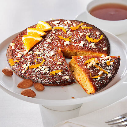 G&acirc;teau &agrave; l&rsquo;orange et aux amandes sur plat &agrave; g&acirc;teau, sucre glace, zestes d&rsquo;orange et part d&eacute;coup&eacute;e