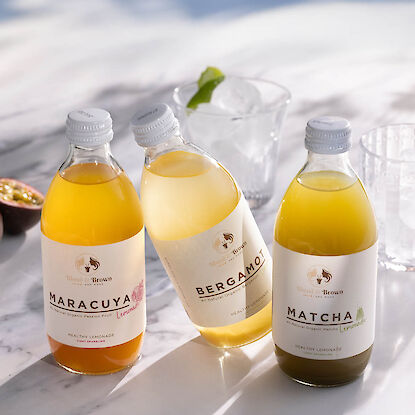 Trois bouteilles de limonade bio aux saveurs maracuja, bergamote et matcha, pos&eacute;es sur table avec verres